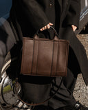 Person holding a brown leather briefcase with a car in the background