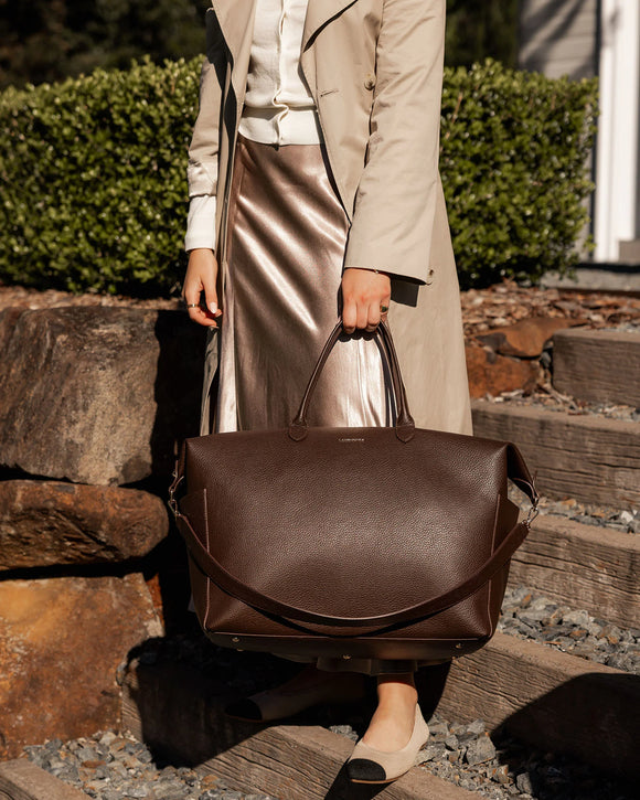Person holding a brown leather bag outdoors on stone steps