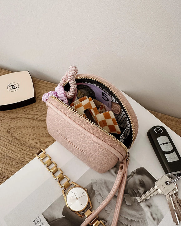 Pink Faux leather pouch with items on a magazine, next to a watch and keys.