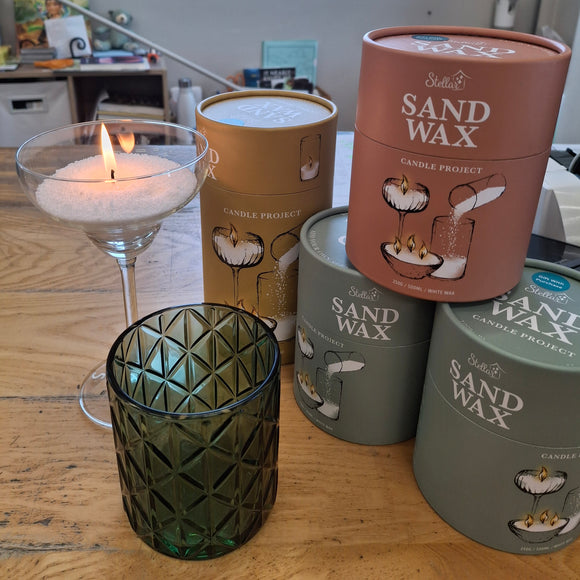 Sand wax candle project with containers and a lit candle on a wooden surface.