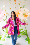 Woman wearing a colorful floral jacket standing in front of large flowers.