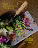 Book titled 'The Floral Dream' with gardening tools and flowers on a wooden surface, promoting a guide to growing cut flowers in New Zealand.