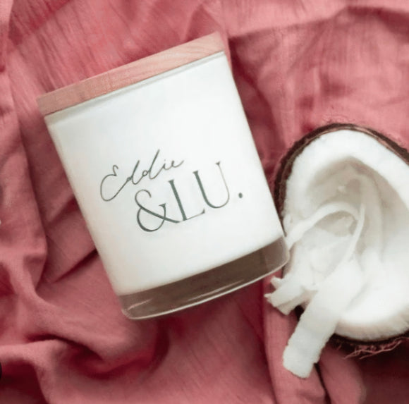 Candle with 'Eldre & Lu' branding on a pink fabric background